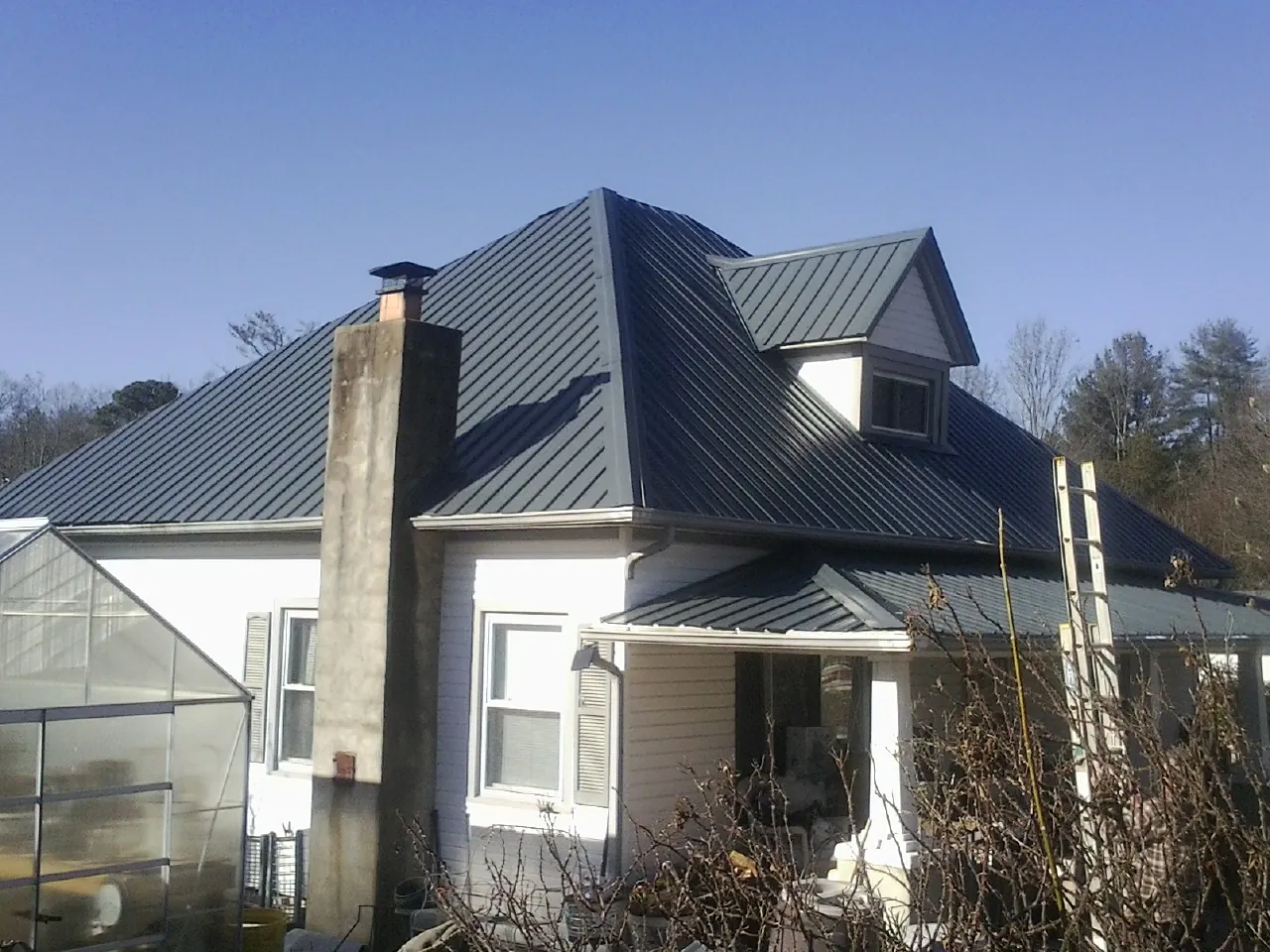 Dark blue standing seam metal roof on a white farmhouse with dormer — Slate & Tile Roof Repair by Roofing Brothers in Statesville