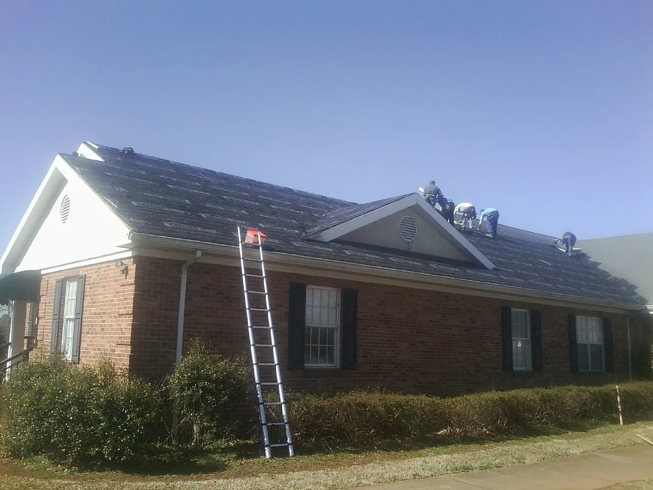 Crew tearing shingles off a brick ranch roof with a ladder set — Metal Roof Repair work by our crew in Statesville