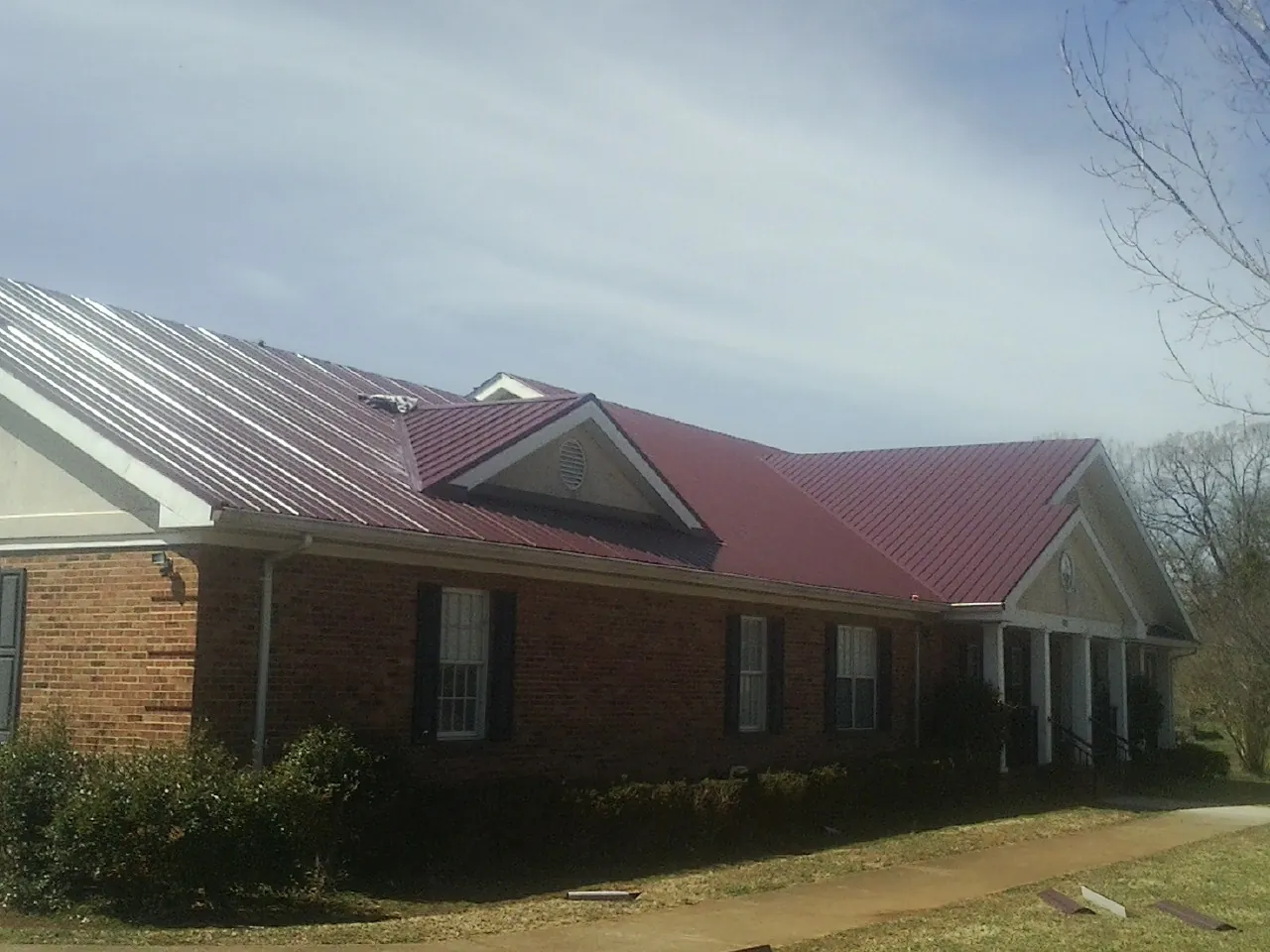 Red metal roof with gabled entries on a long brick building, from a Hail Damage Roof Repair job in Statesville