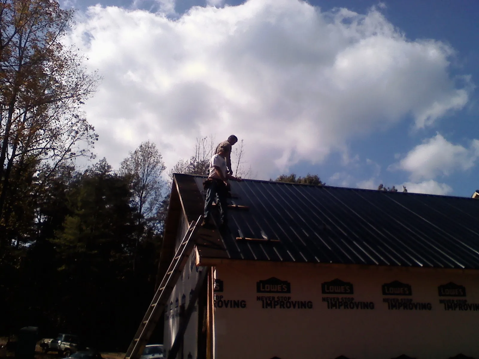 Roofer fastening dark metal panels high against a cloudy sky, from a Roof Inspection job in Statesville