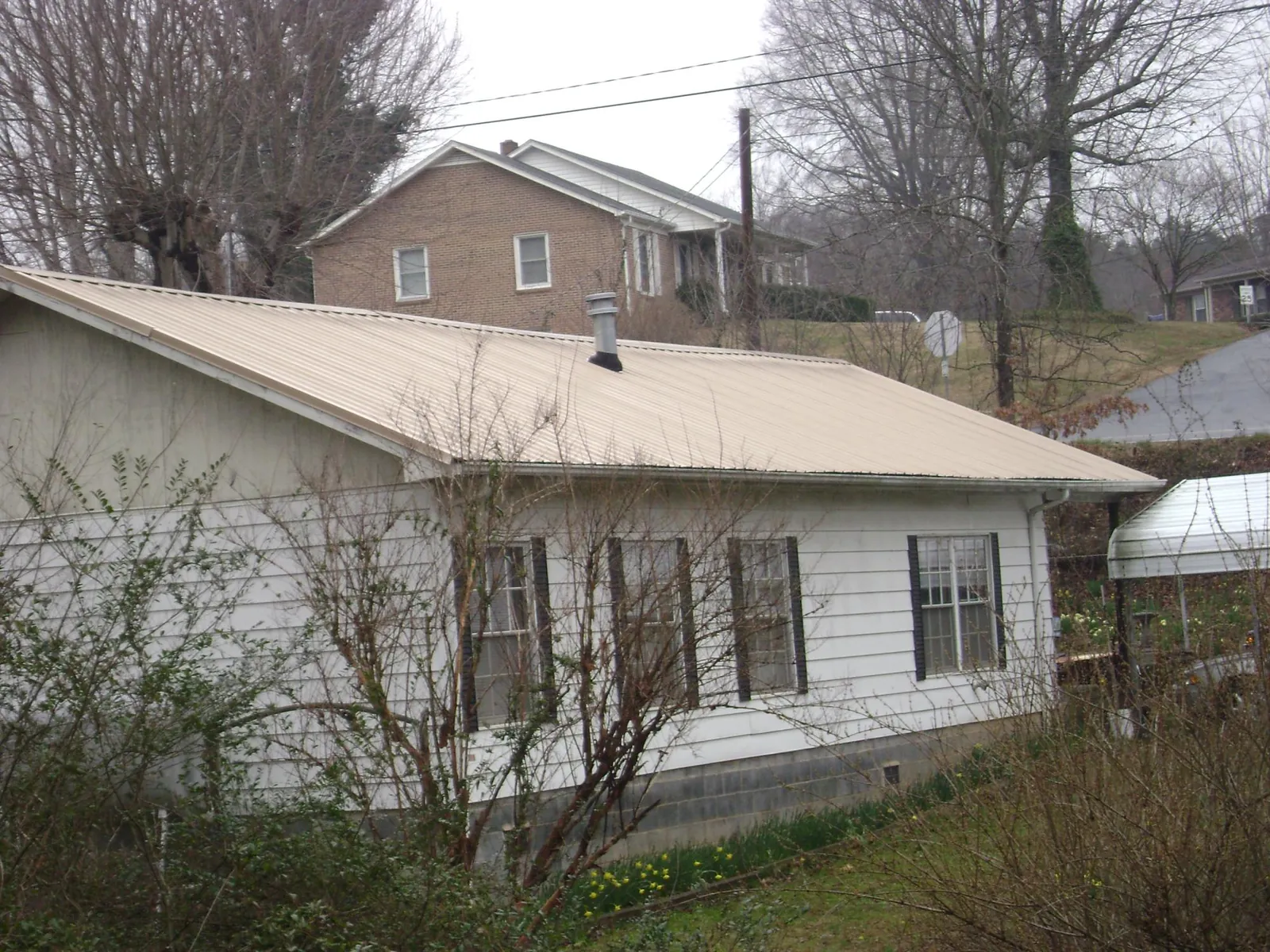 Tan metal roof on a white sided house set into a hillside — Commercial Roofing by Roofing Brothers in Statesville