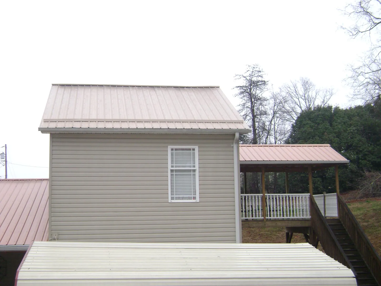 Tan metal roofs on a two story addition and attached porch, from a Roof Replacement job in Statesville